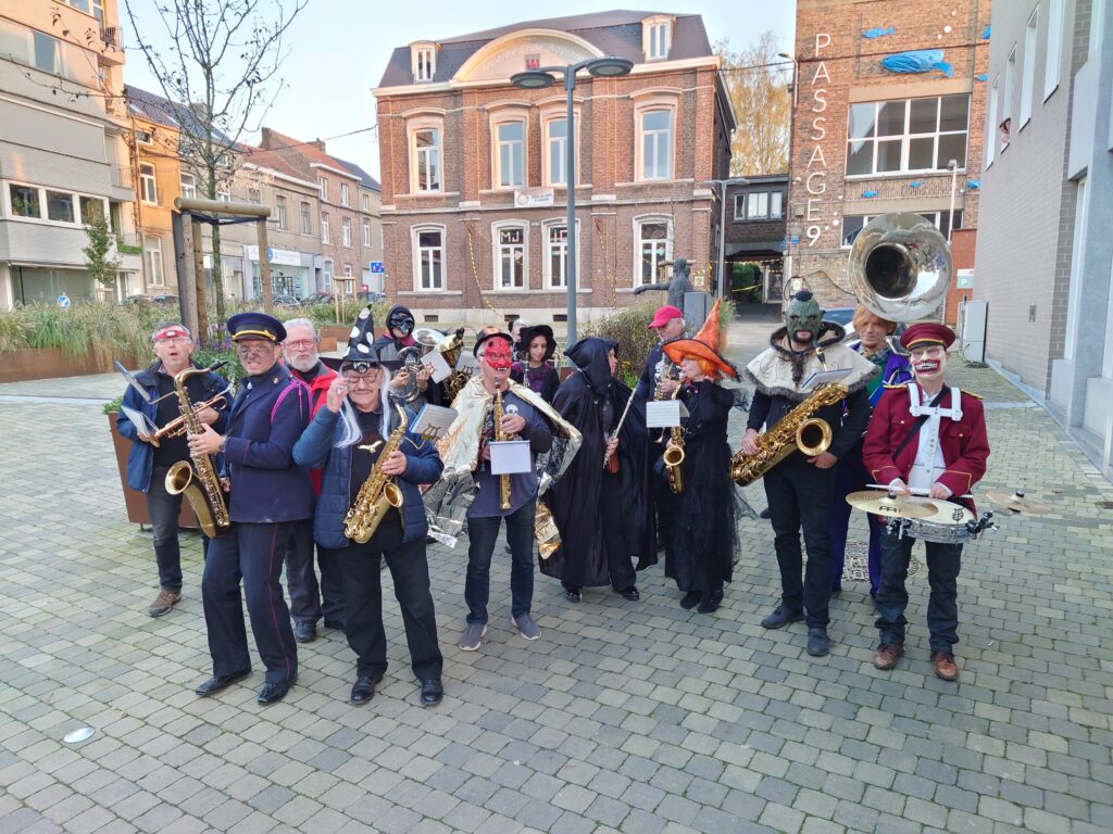 Pour le Conte et Cortège d’Halloween à Waremme, l’Ensemble Instrumental Waremmien s'est plongé dans l'ambiance en adoptant des costumes effrayants et fantastiques. Les musiciens, déguisés en sorcières, monstres et autres personnages d’épouvante, ont accompagné les festivités avec des mélodies sombres et festives, ajoutant une touche musicale à l’atmosphère mystérieuse de cette célébration. Dans un décor urbain devant le Passage 9, l’orchestre a su captiver l’attention et divertir les participants du cortège.